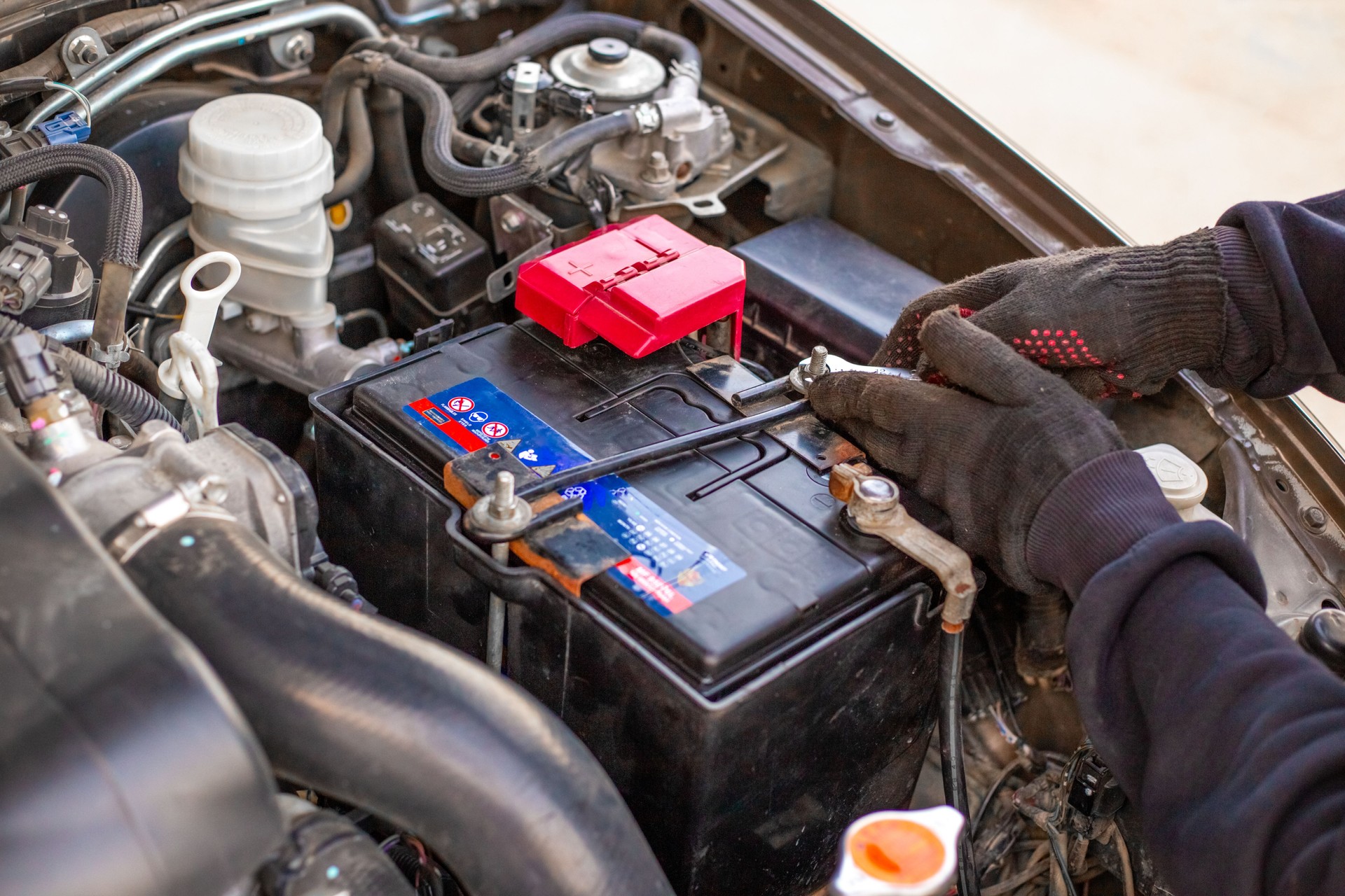 A man wearing gloves securely fastens a car battery terminal after installing it under the hood. Replacing a weak battery